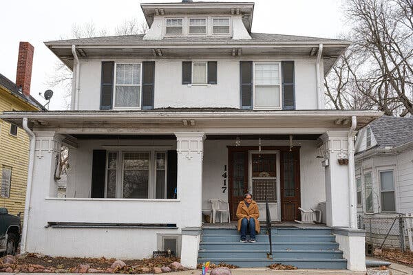 In a camel-colored long coat and jeans, Gay Glenn sits on the steps on the porch of her mother’s two-story house in Kansas.