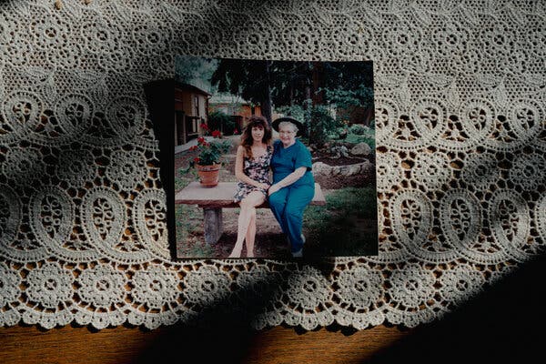 A snapshot of Annie Reid in a floral dress and her mother, Frances Sampogna, sitting on a bench outside. The photograph rests on a lace doily.