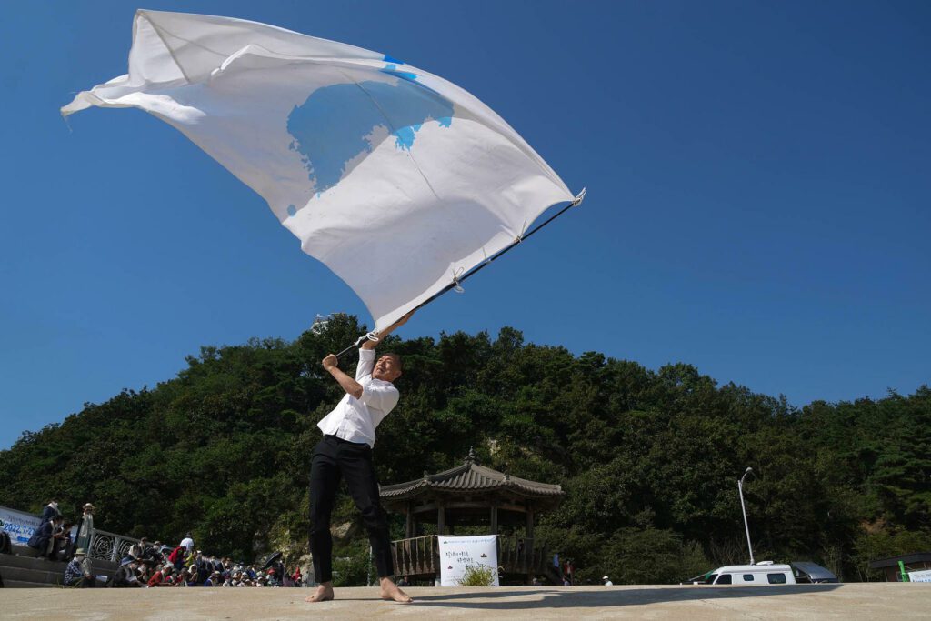 Lee San Hun, an artist, dances with a flag that symbolizes a unified Korean Peninsula, in Ganghwa-do, South Korea on Sept. 21st, 2022. He was among people gathered on the anniversary of the Korean War armistice in 2022. (Chang W. Lee/The New York Times)