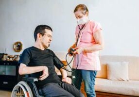 Serious disabled young man at home with nurse
